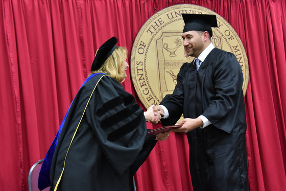 Chancellor Mary Holz-Clause handing a diploma to a student