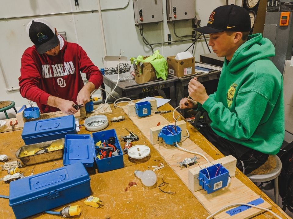 Two male students learning how to wire electrical boxes