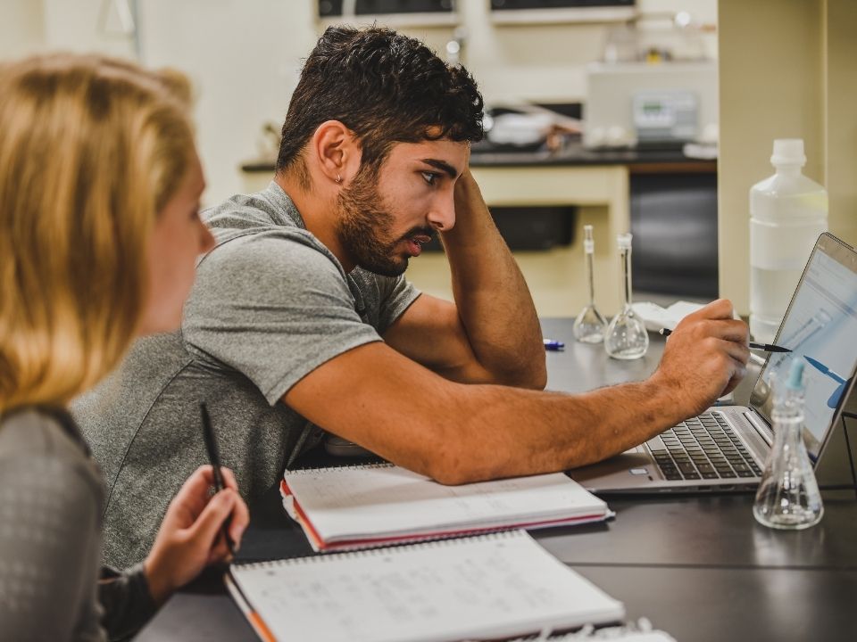 Two students looking at a computer and writing notes down in a lab