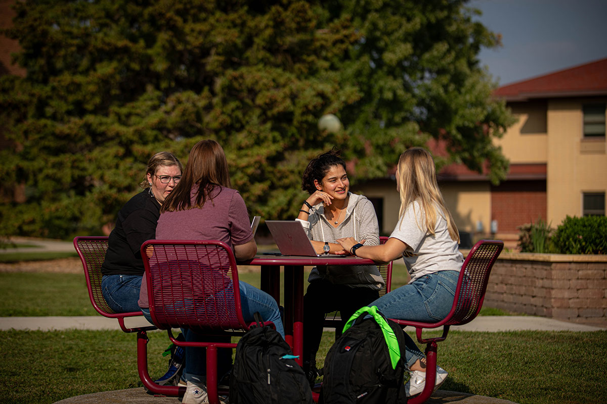 Four students having a conversation outside at a table.