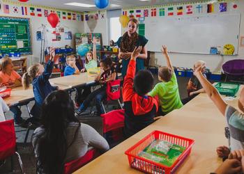 Student teacher in a local classroom with kids excited and raising their hands