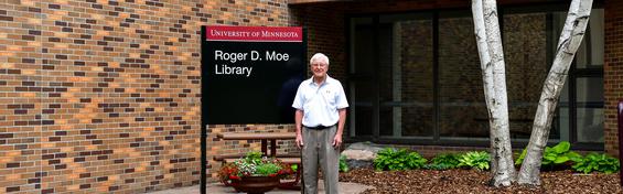 Roger D. Moe outside the library building next to the new Roger D. Moe Library sign