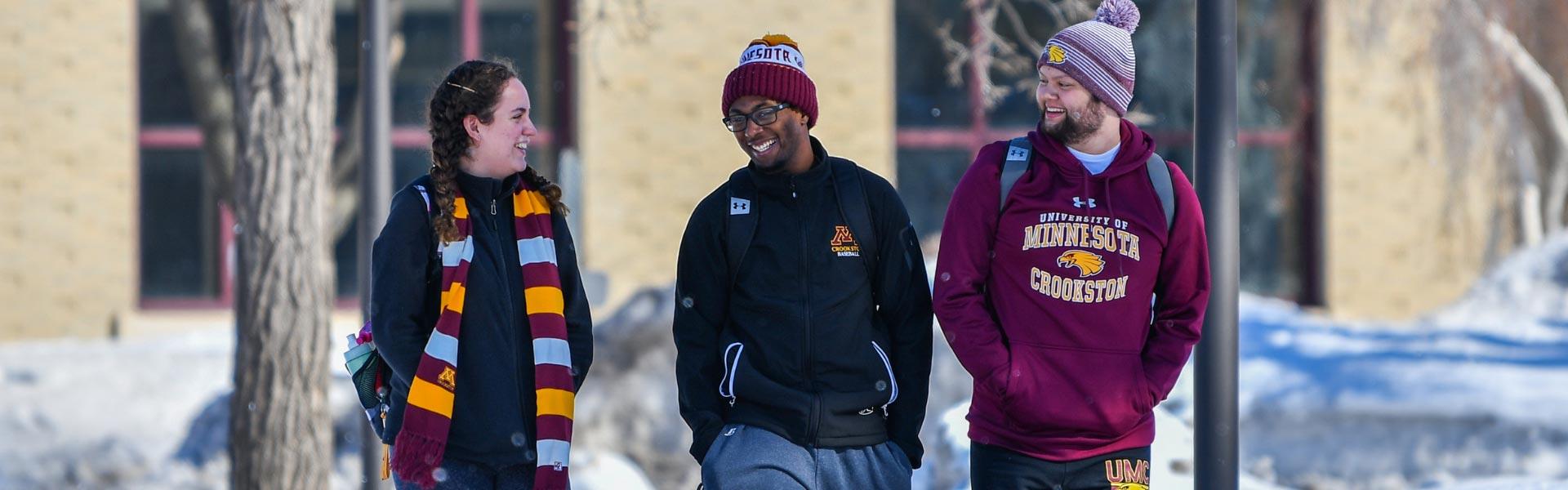 Three students walking outside the student center in the winter, laughing and chatting