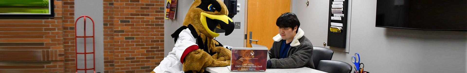 Student employee helping Regal the Eagle with his laptop in the Computer Help Desk Lobby
