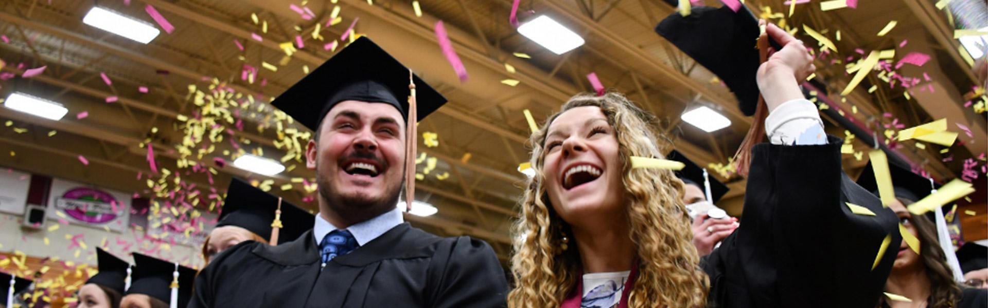 Two students at commencement with confetti and huge smiles