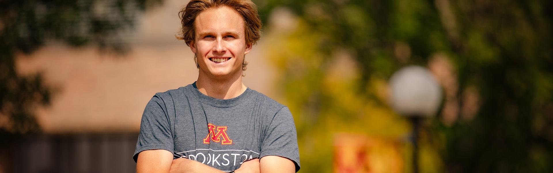 Male student standing with arms crossed with UMN Crookston tshirt during the fall