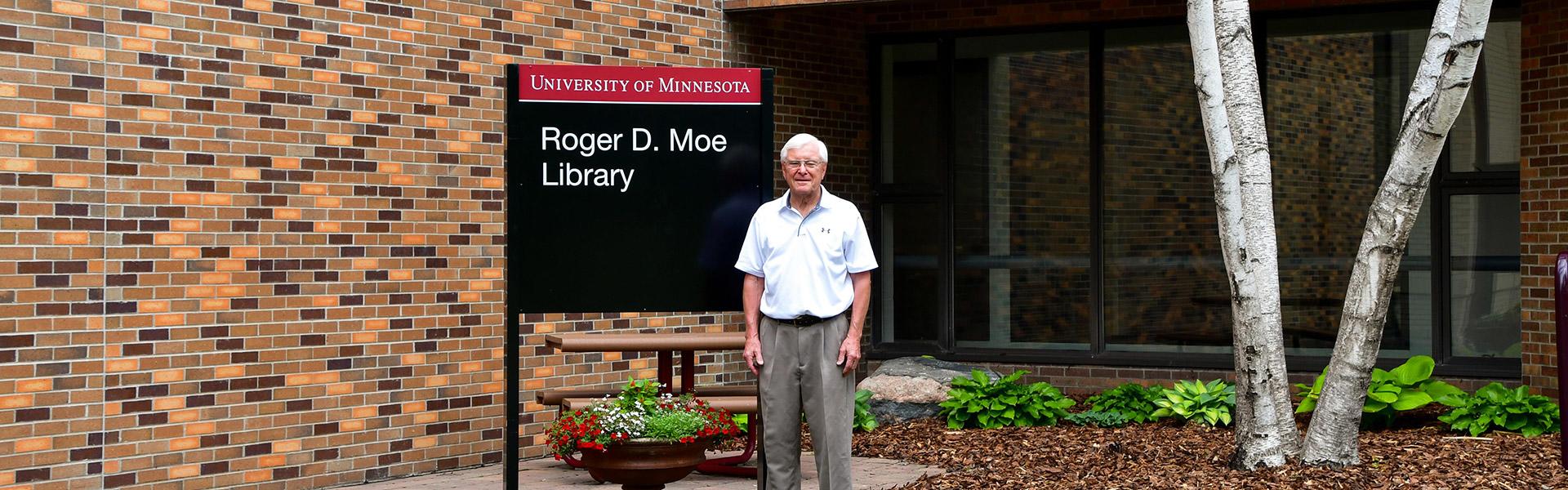 Roger D. Moe outside the library building next to the new Roger D. Moe Library sign