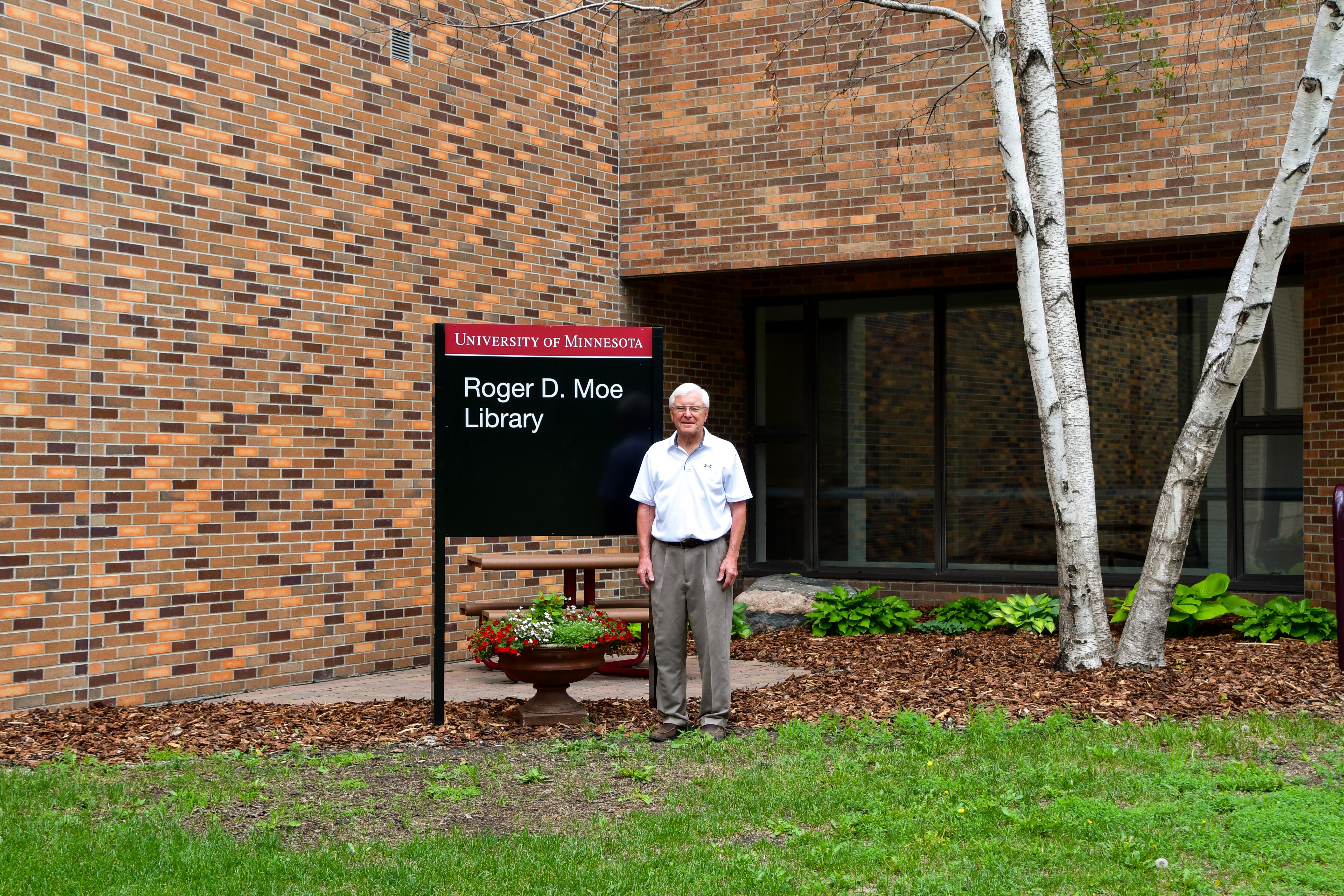 Roger D. Moe stands in front of the sign for the Roger D. Moe Library