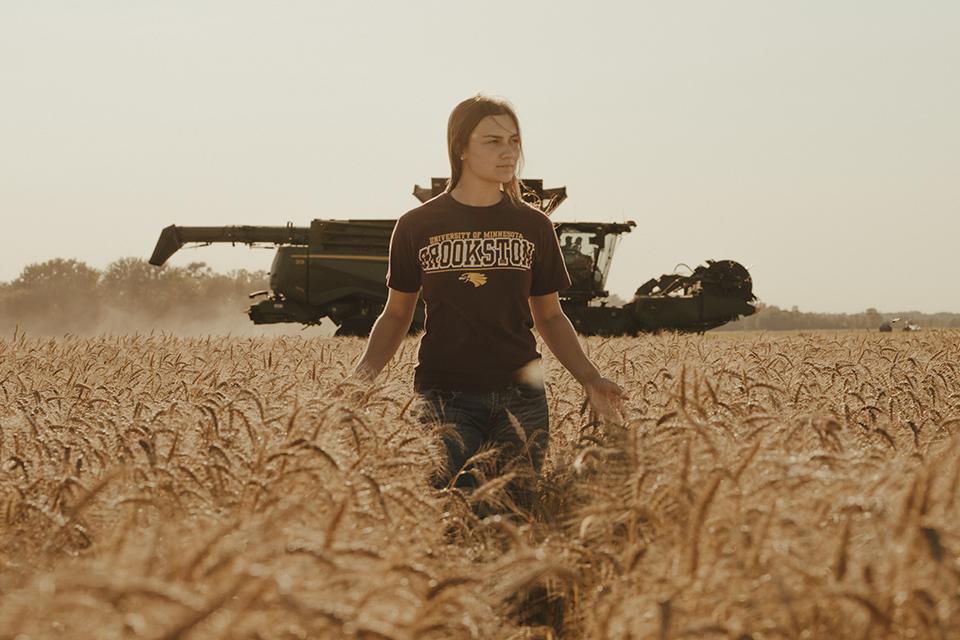 Female agricultural student standing in a ripe wheat field with a combine in the background