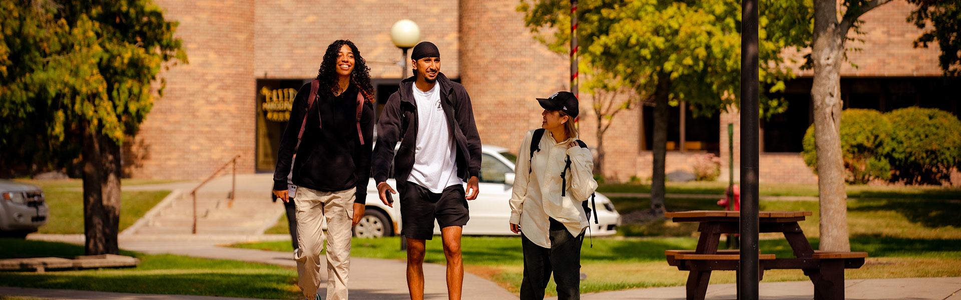 Three students walking and talking on the Campus Mall in front of Sahlstrom Conference Center