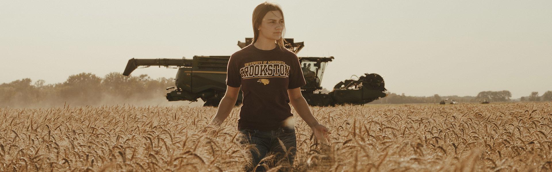 Female Agriculture student standing in a wheat field with a combine in the background
