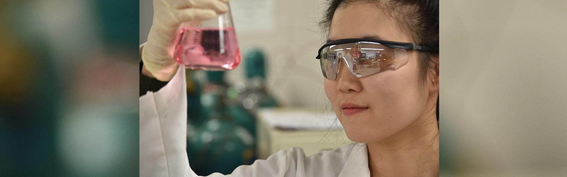 Student holding a beaker of chemicals at eye level in a chemistry lab