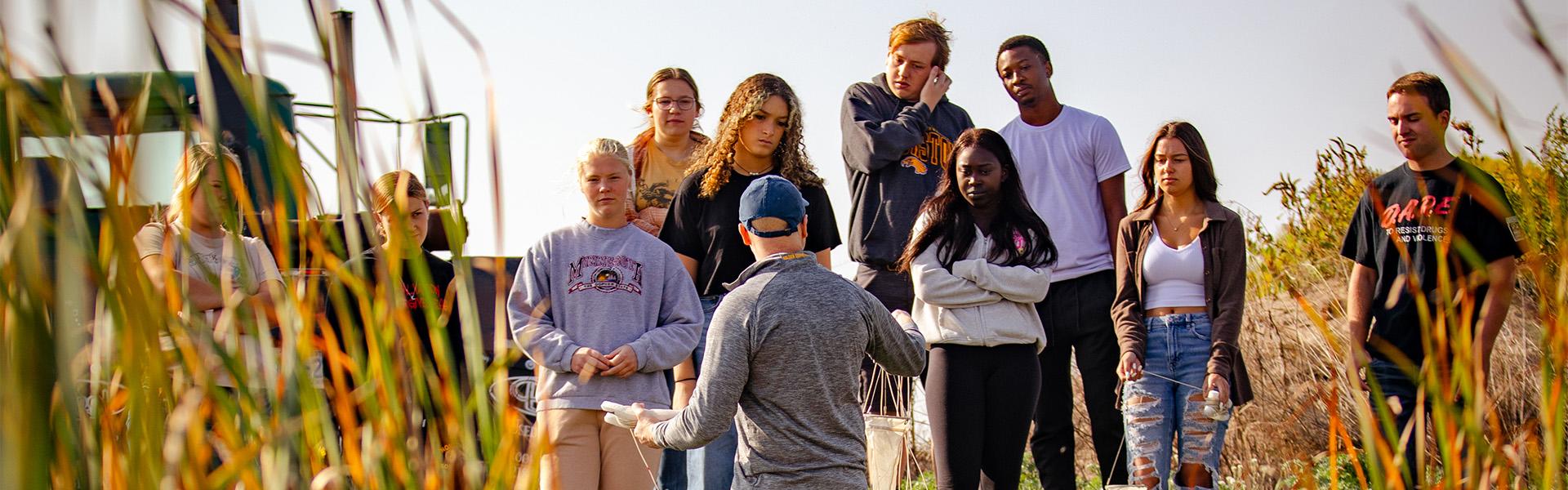 Biology professor with a group of students on a sunny fall day taking them down to a pond to take samples