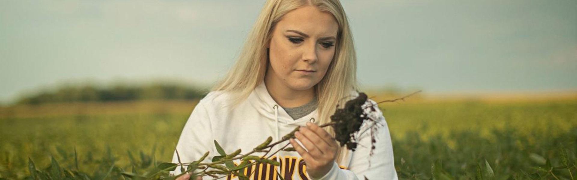 Britton Fuglseth holding a plant in a field and looking at the roots