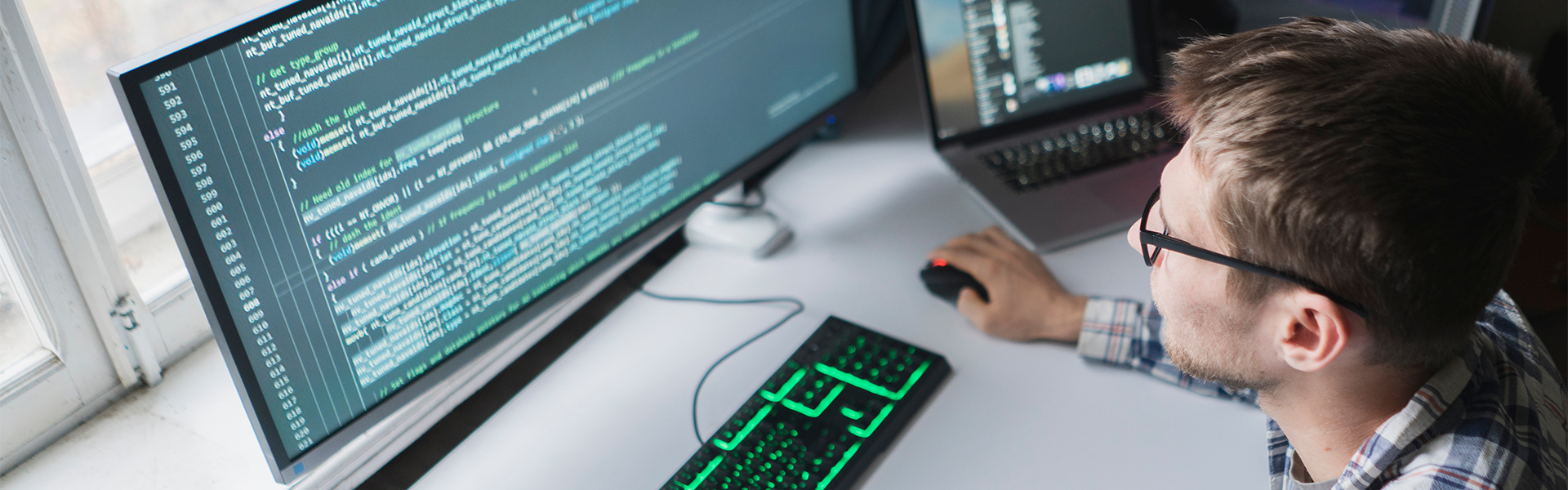 Male with glasses working on a desktop and laptop computer