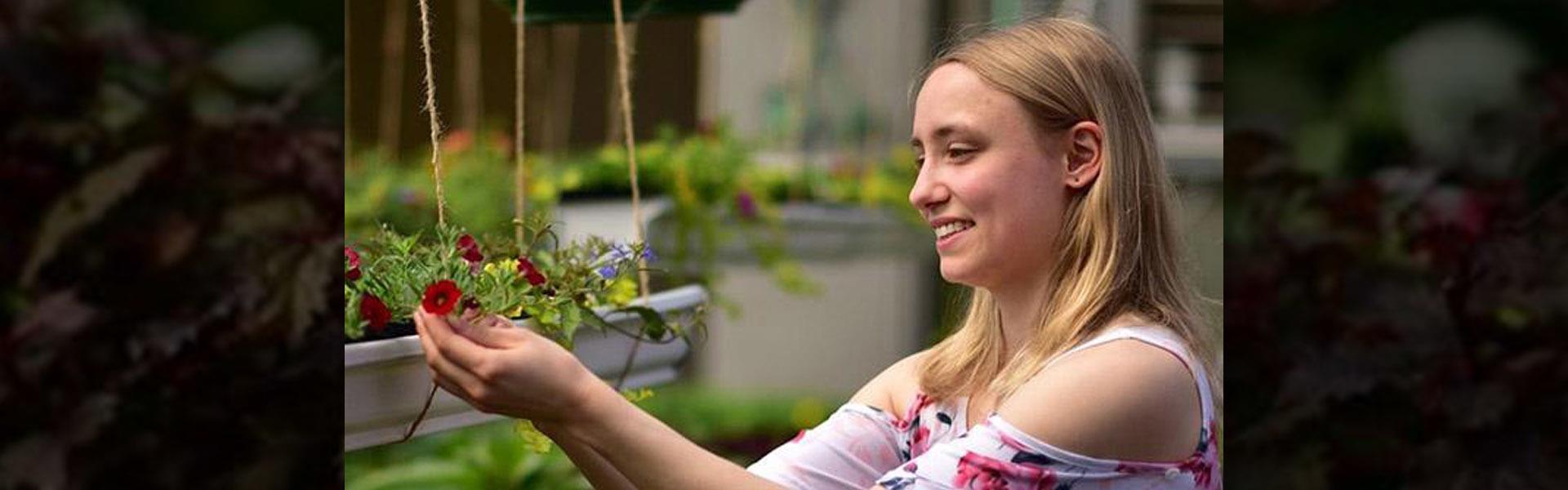 Heidi Reitmeier carefully looking at a flower in the greenhouse with the sun shining on her face