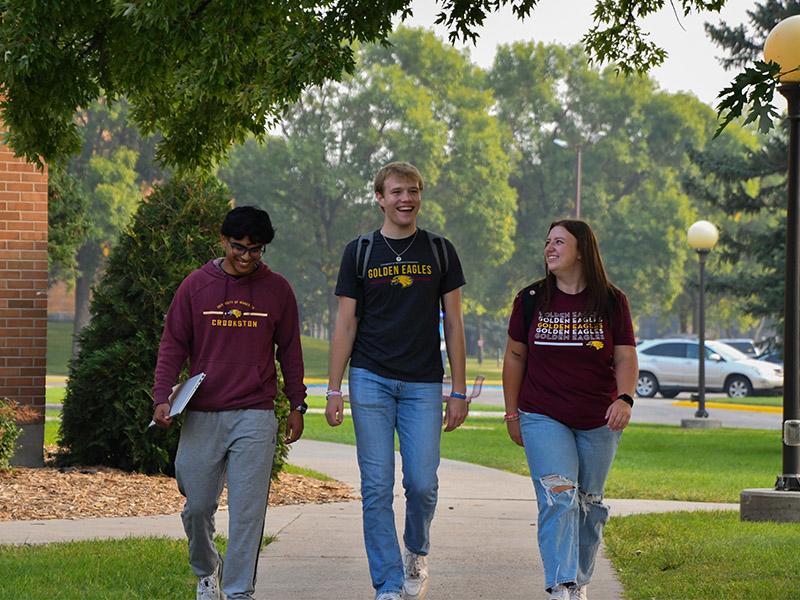 Three UMC students walking and talking on the Campus Mall during early fall