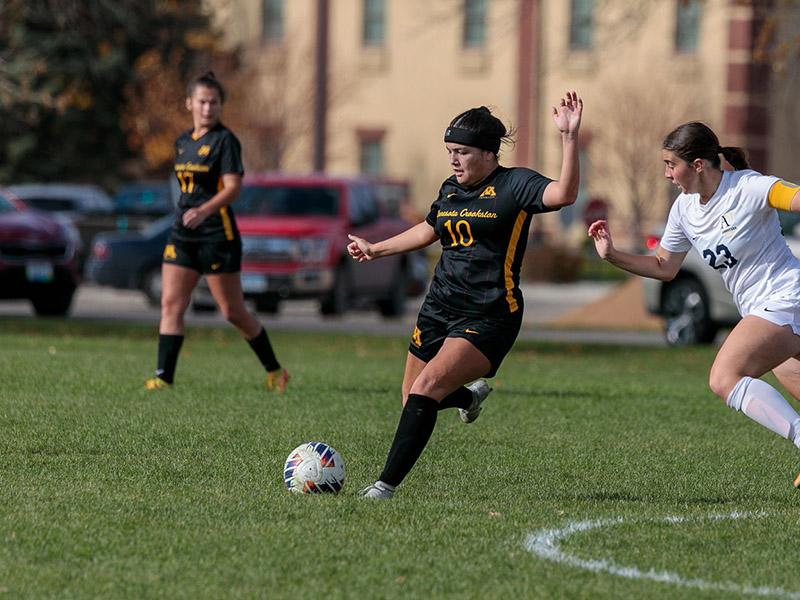 U of M Crookston soccer player in a black jersey kicking the ball during a game