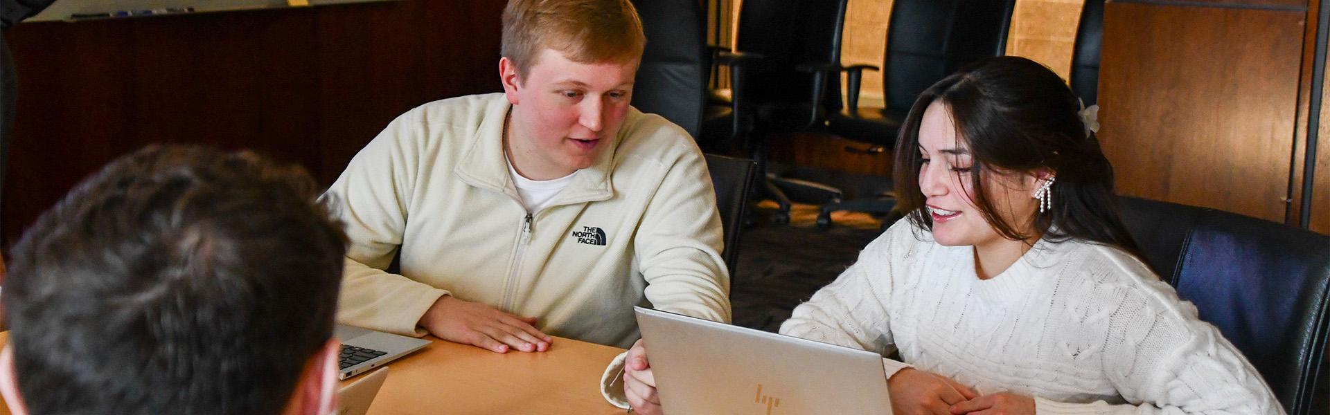 Three students talking and working on laptops in the Business Boardroom