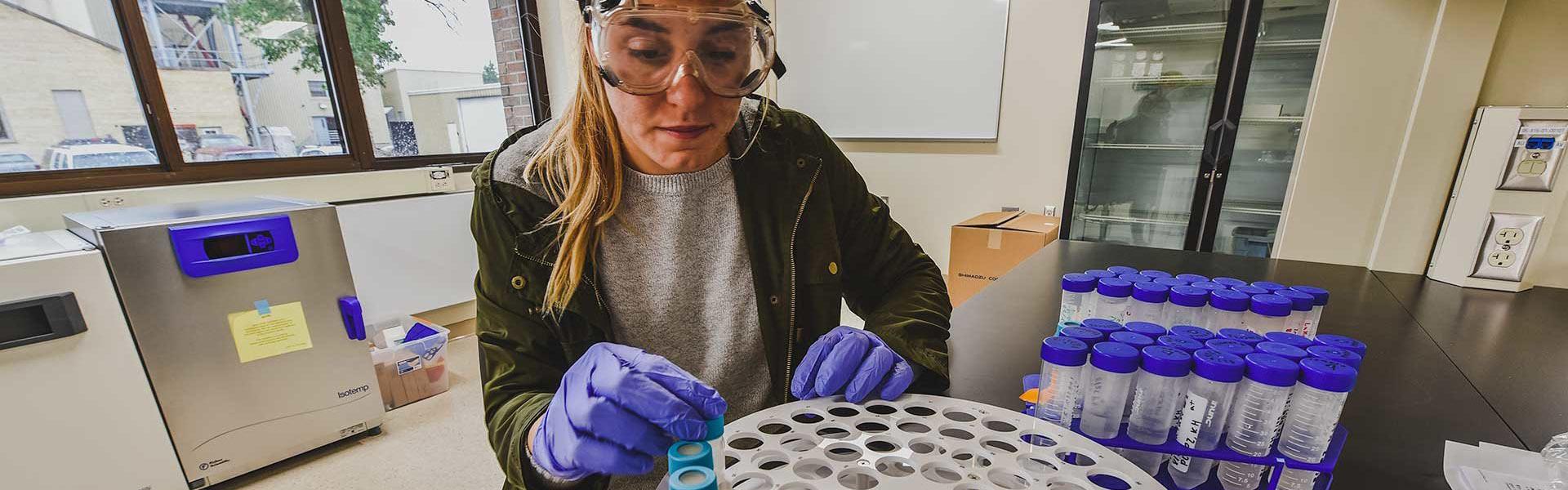 Student, wearing protective googles and gloves, working in the UMC lab with a centrifudge