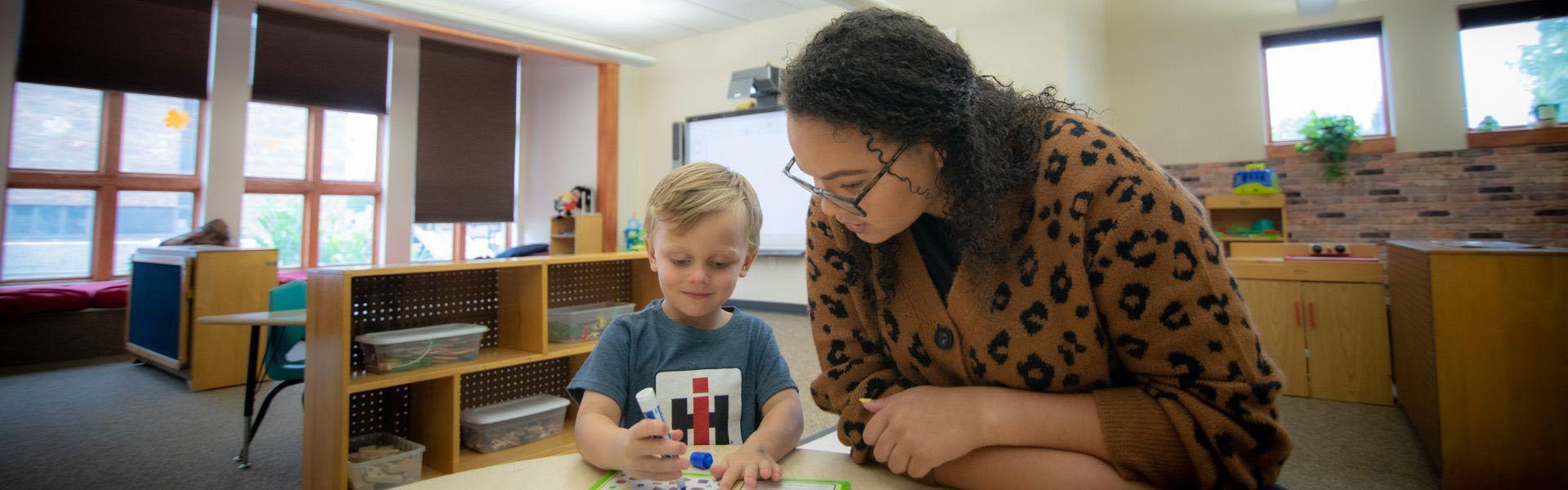 Photo of a teacher helping a child draw. 