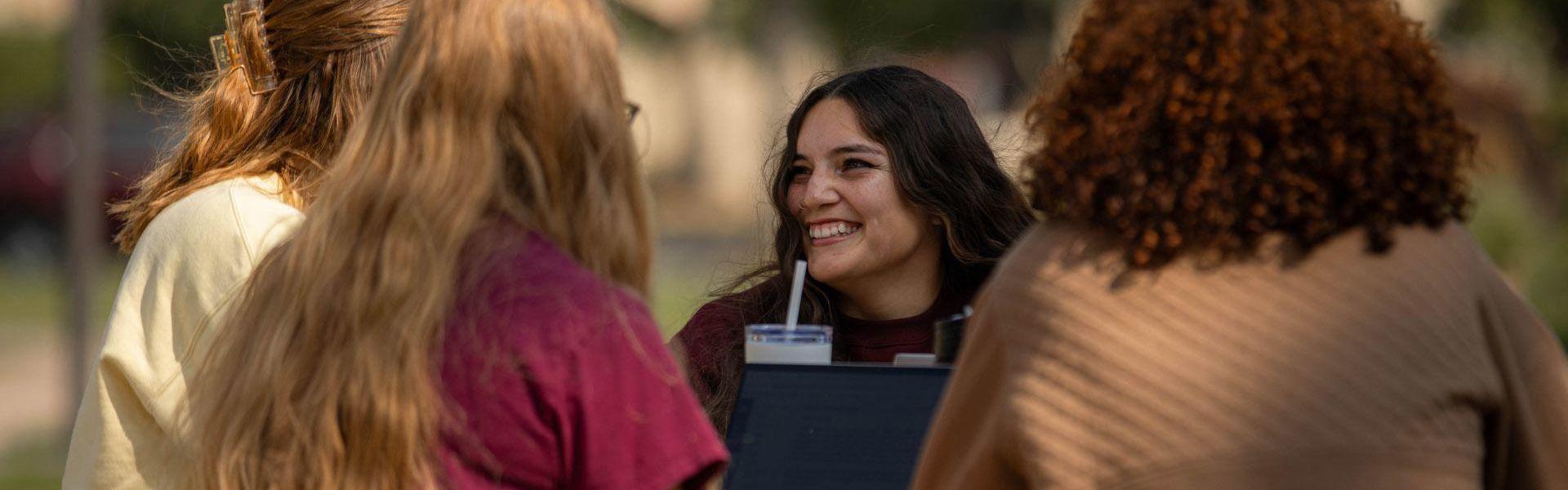 Four female students sitting outside at a picnic table laughing and talking during late fall on the Campus Mall