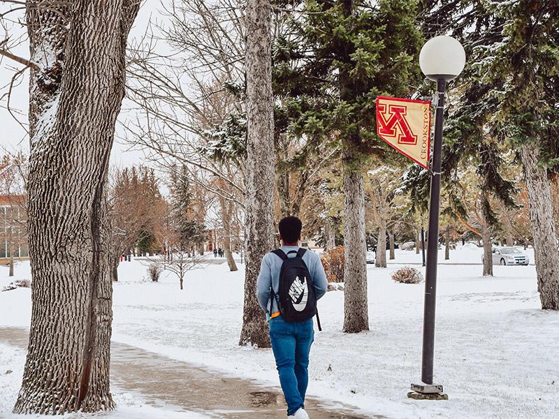 Student walking down the Mall sidewalk with a light jacket with freshly fallen snow