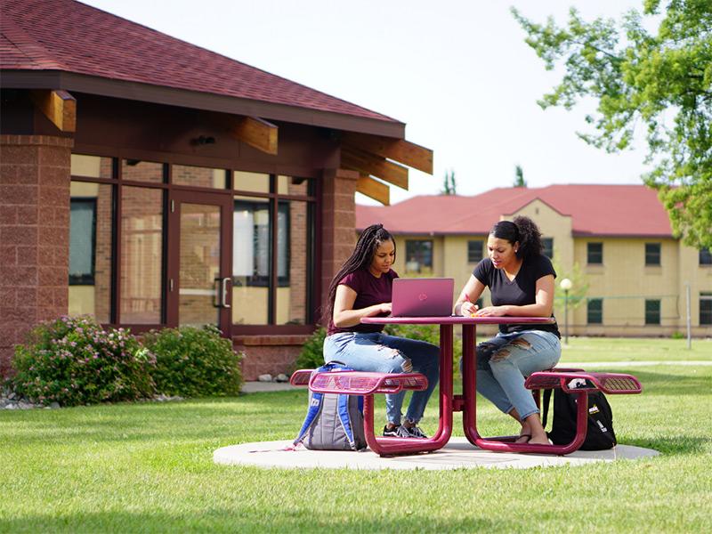 Two students sitting outside during the summer next to Evergreen Hall and Evergreen Grill