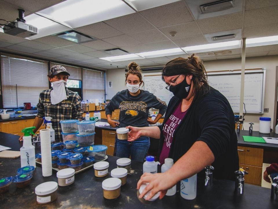 A faculty member and students in a lab looking at jars of different turf grasses and soils