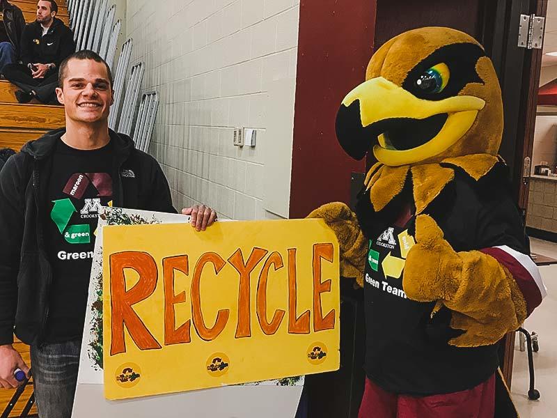 Regal the Eagle and a student holding a Recycle sign in Lysaker Gymnasium during a game