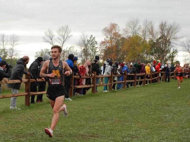 Golden Eagle men's cross country runner on a grass path outfront