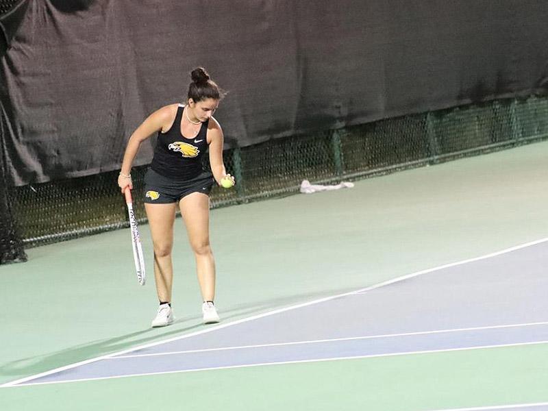 Player dribbling the tennis ball before beginning their serve on an outdoor court