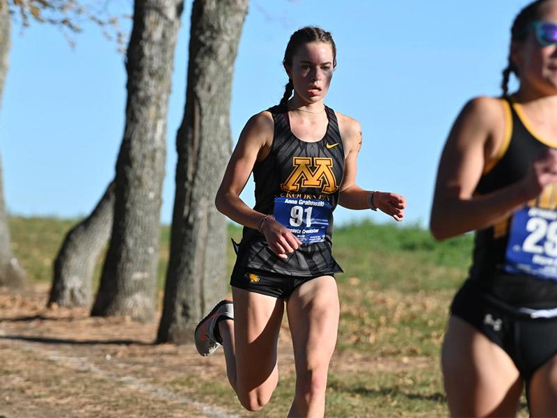 Golden Eagle women's cross country runner on a trail on a sunny day