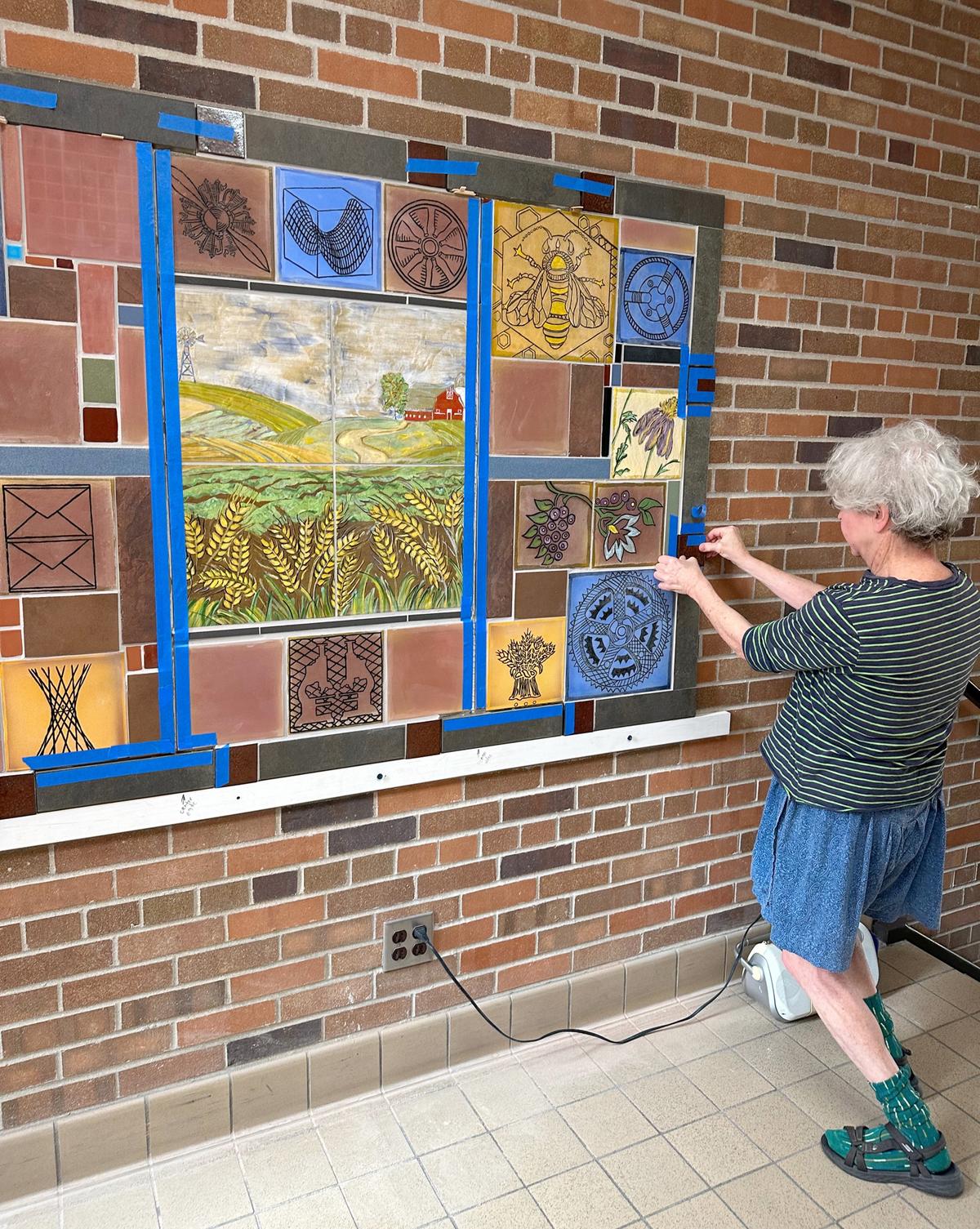 Artist Susan Warner works on the installation of the tile art in Dowell Hall
