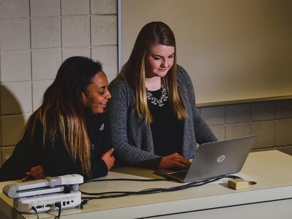 Two female students sitting in a classroom working on a project