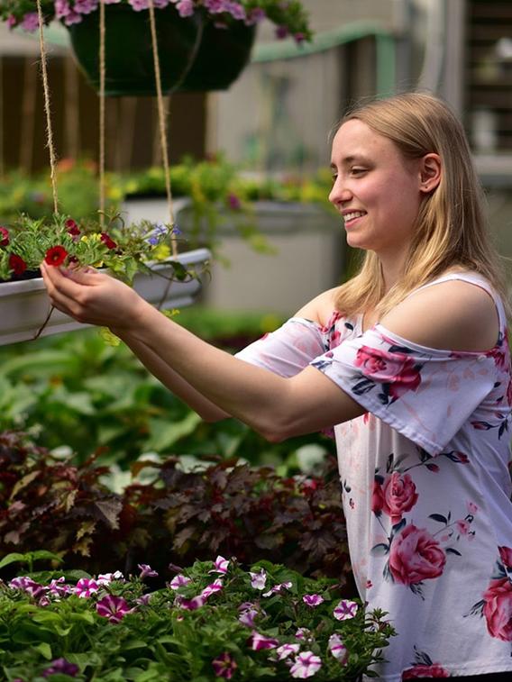 Heidi Reitmeier carefully looking at a flower in the greenhouse with the sun shinig on her face