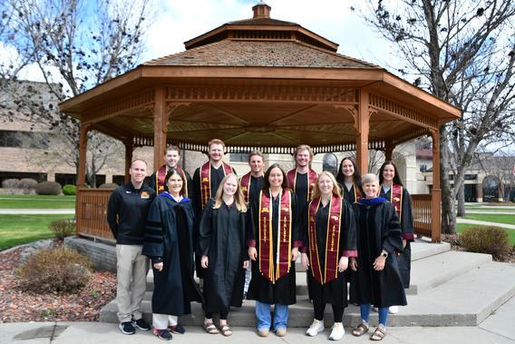 A group of students in their gowns at Commencement standing in front of the Peterson Gazebo