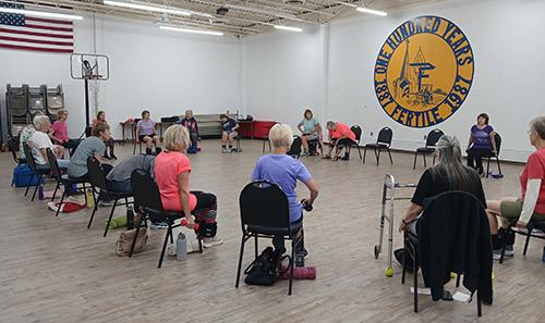 Seniors sitting in a circle on chairs with dumb bells doing workouts in Fertile MN