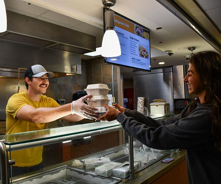 Server handing stacked takeout boxes to a customer at a counter.