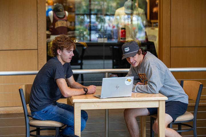 Two students having a conversation while looking at a laptop