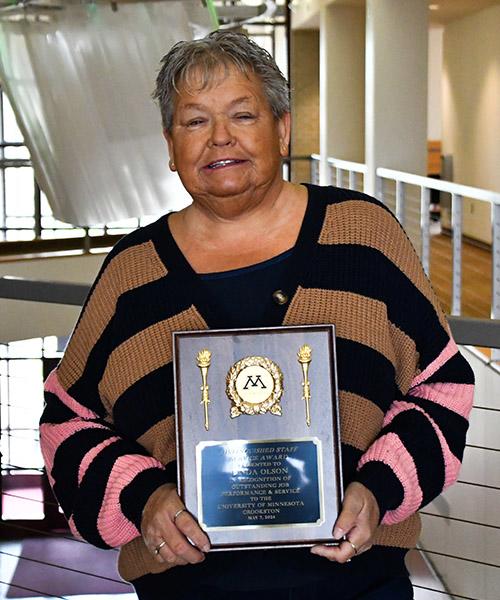 Linda Olson holding her Distinguished Staff award plaque outside of the Northern Lights Lounge