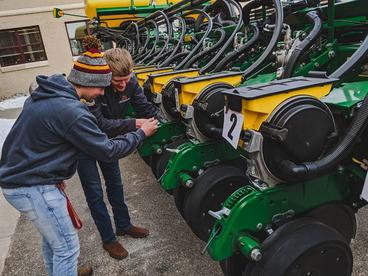 Two male students working outside on a row planter