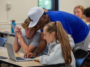 Three students working together on a laptop in a classroom