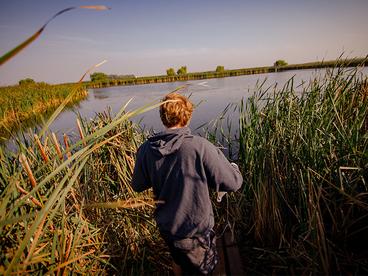 Student walking down through reeds to get to a pond