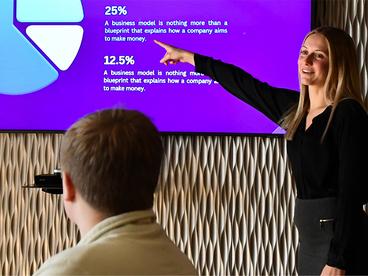 Female student in front of her classmates giving a business presentation in the Business Board Room