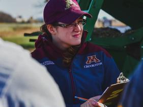 Ag student standing in a field outside a combine with a clipboard listening and taking notes