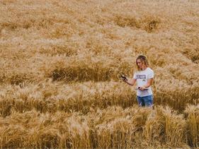 Female student standing in a wheat field with a clipboard and a GPS device