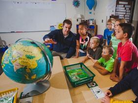 Elementary Education student teacher in a classroom with third graders looking at a globe.