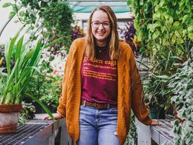 Student in the campus greenhouse with a big smile wearing a Golden Eagle tshirt