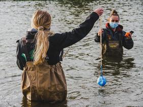 Two students waist deep in river water taking samples